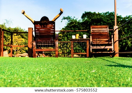 happy woman feel comfortable and relaxing on wooden sun bed furniture outdoor on green artificial grass and looking the blue sky background, coffee morning concept Royalty-Free Stock Photo #575803552