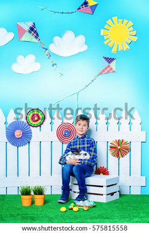 Happy child boy with Easter Bunny and painted eggs in spring decorations. Kid's fashion. Easter holidays.