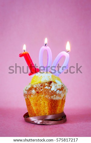 Muffin with burning birthday candles as number one hundred on pink background