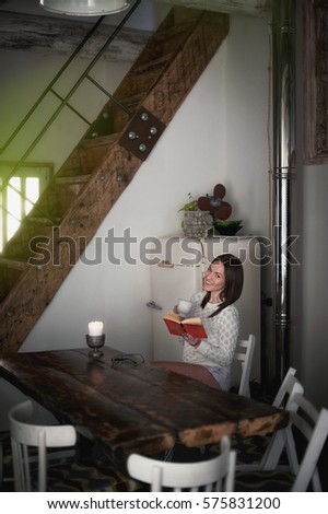 Amazing girl in a studio loft. Beauty in a white sweater and shorts, empty flat, white interior. Brunette in denim shorts and a white sweater. girl sitting and reading a book, drinking tea