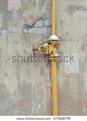 Yellow gas tube with valve on the background of gray shabby wall. Caption: "Gas".