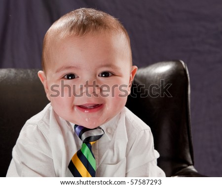 Beautiful smiling baby boy sitting in a leather chair wearing a colorful neck tie
