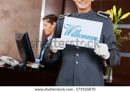 Page at hotel reception holding German sign saying "Willkommen" (welcome)