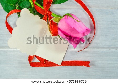 Pink rose and blank greeting card is on plank wood background, for Valentine's day.