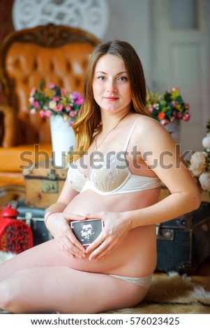 happy pregnant girl, sits on a floor and holds the first picture of the kid near a tummy. Motherhood