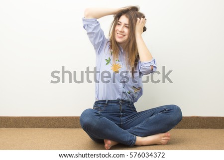 Beautiful girl dressed in blue shirt smiling and sitting on the floor