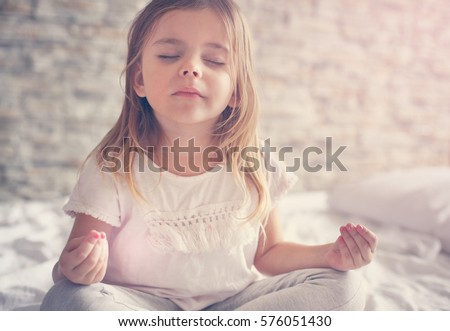 Little girl doing yoga in bed.  Royalty-Free Stock Photo #576051430