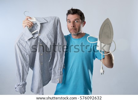 young attractive and frustrated man holding iron and shirt stressed and tired in bored and lazy face expression in male ironing going wrong and domestic work concept isolated even background