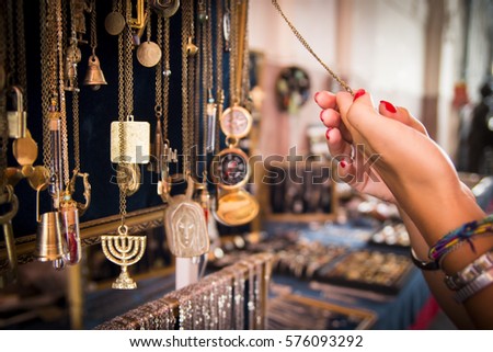 Close up of a golden charm Jewish souvenir Menorah. Woman hands with red nail polish holding a pendant. Choosing a present.