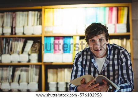 Portrait of smiling student reading book in the college library