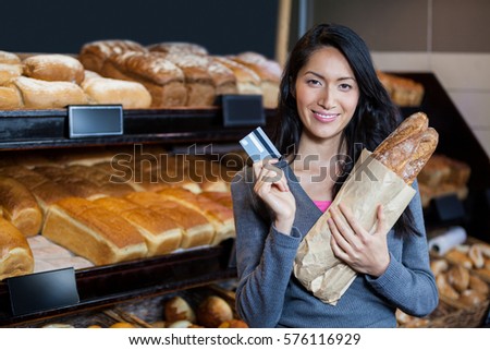 Portrait of smiling woman holding baguettes and credit card at bread counter of supermarket
