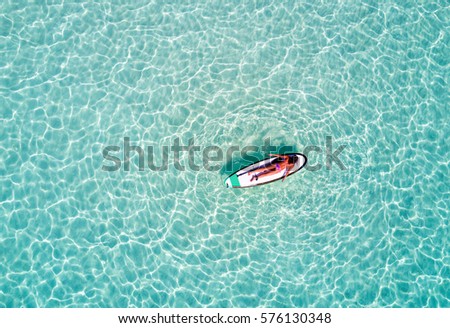 Aerial picture of a woman on a surfboard in turquoise waters