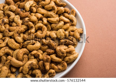 A handful roasted spiced cashew nuts  or masala kaju served in white dish, selective focus