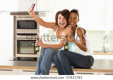Two Girlfriends Taking Photo With Digital Camera In Modern Kitchen