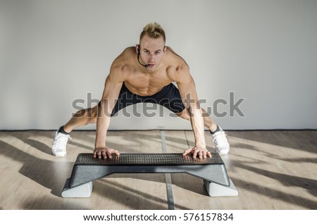 Young aerobics male coach shirtless leaning on step teaching class, looking at camera