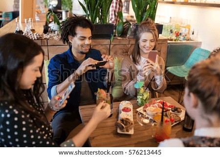 technology, lifestyle and people concept - happy friends with smartphones taking picture of food at restaurant
