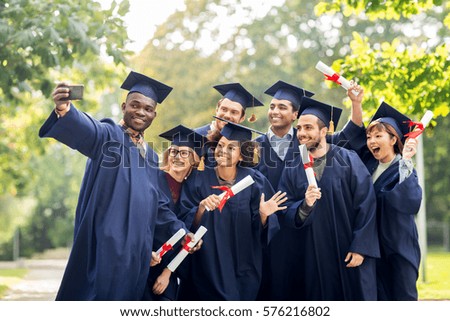 education, graduation, technology and people concept - group of happy international students in mortar boards and bachelor gowns with diplomas taking selfie by smartphone outdoors Royalty-Free Stock Photo #576216802