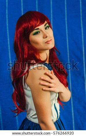 the girl of Asian appearance , in a red wig and blue dress . the anime style. Girl posing on blue background