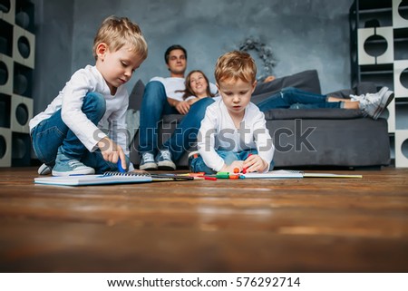 Children draw markers on floor while parents relax couch
