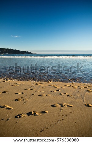 portrait view on sandy beach with feet traces and atlantic ocean with blue sky in sunset