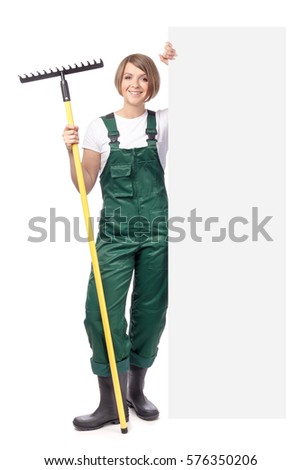 young smiling woman professional gardener with rake standing next to the banner with empty copy space isolated on white background. advertisement blank board. gardening service and business concept