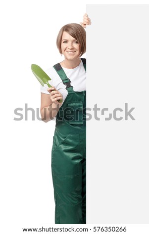 young smiling woman professional gardener with trowel standing next to the banner with empty copy space isolated on white background. advertisement blank board. gardening service and business concept