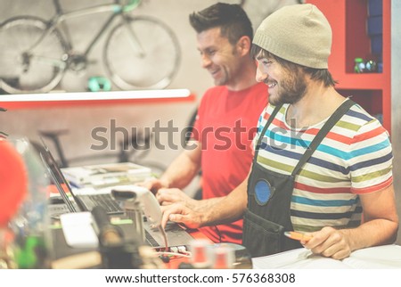Two bicycle repairer colleagues working in bike garage - Positive mood bmx seller using computer in workshop  - Retail selling and sport trend concept - Focus on right man face - Warm filter