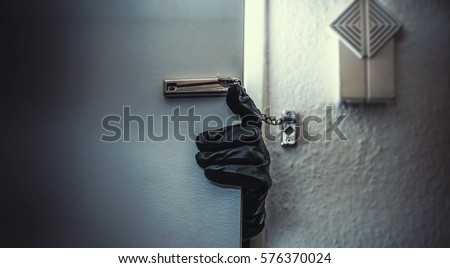 masked burglar with crowbar breaking and entering into a victim's home  Royalty-Free Stock Photo #576370024