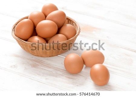 Brown chicken eggs, most in a woven wicker basket and three on wooden panel surface