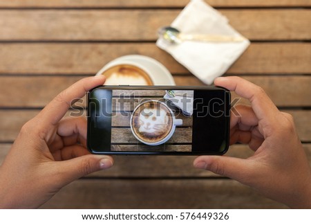 close-up hand holding phone taking coffee photo on table