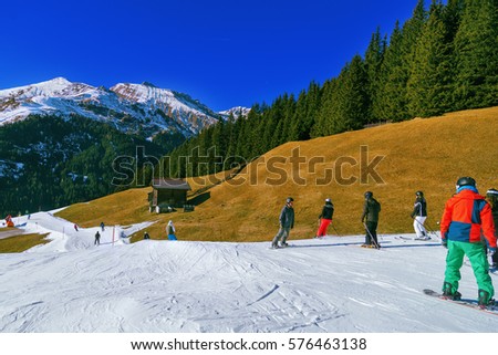 Active holidays skiing in the Alps. Mountain peaks covered with snow in the background. Skiers descend down the hill. Alps with green pine trees and clear blue sky.