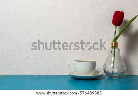 Workplace with coffee cup, plants on blue table. White wall
