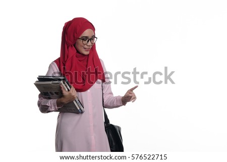 A pretty young muslim lady / woman with hijab is carrying her book and bag which pointing her finger at an empty space isolated on white background