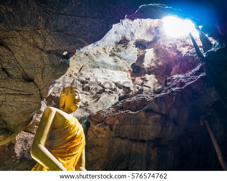 Golden Buddha statue with sun ray in cave in deep forest