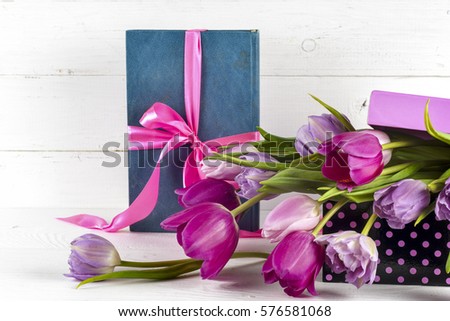 Gift, purple tulips and book over wooden table.