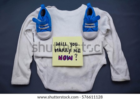 Baby clothes and will you marry me now text on a note