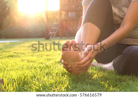 Foot pain .Woman sitting on grass Her hand caught at the foot. Having painful feet and stretching muscles fatigue To relieve pain. health concepts. Royalty-Free Stock Photo #576616579