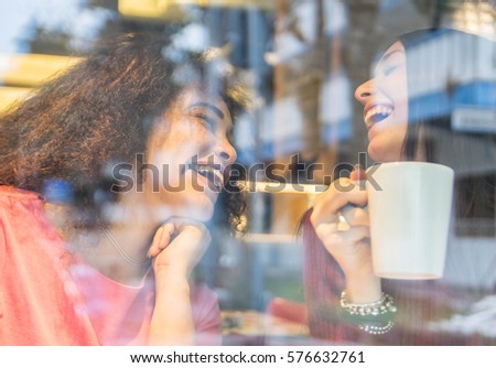 Two happy women laughing drinking tea. Couple of smiling friends having fun behind the glass of a bar.