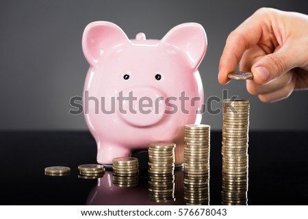 A Person Stacking Coins In Front Of Piggybank Over Gray Background