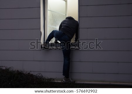 Rear View Of A Burglar Entering In A House Through A Window Royalty-Free Stock Photo #576692902