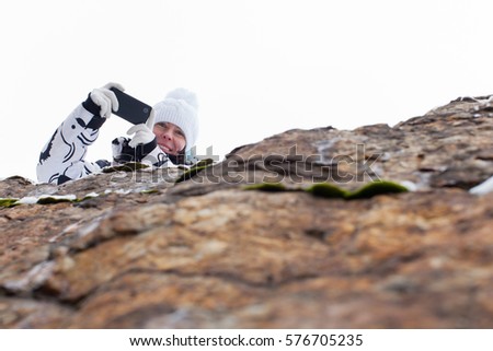 Woman taking mobile phone for pictures on the rock in winter 