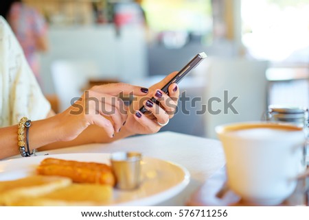 Woman holding mobile phone in hands, texting in social media. Breakfast of business lady.