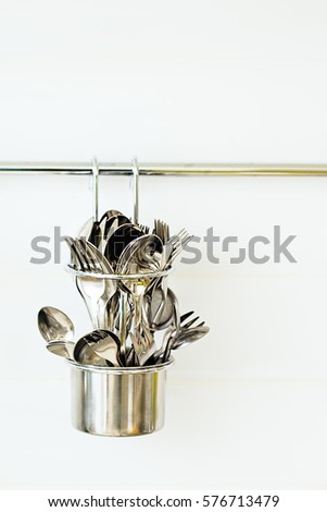 Silverware utensils hanging on rack. Kitchen storage ideas. White background.