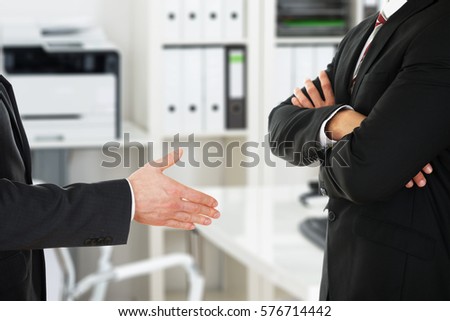 Person Offering Handshake To Businessman With Arm Crossed At Office Royalty-Free Stock Photo #576714442