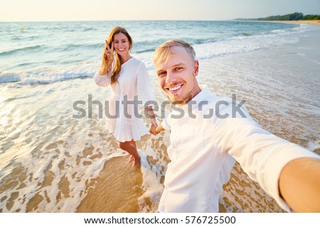 Walking on the sea shore. Pretty young loving couple taking selfie together on smartphone on beach.
