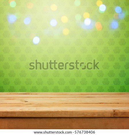Empty wooden deck table over green shamrock wallpaper background with bokeh lights overlay. St. Patricks day concept for product montage display
