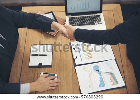 Two businesses are business dealings (business negotiation),business handshake.Wooden desk with a laptop,notebook,tablet,pen and annual reports,working space.