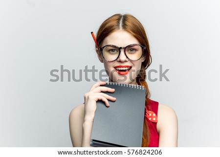 Young woman with a notebook and pencil, white background with glasses, surprised looking at the camera.