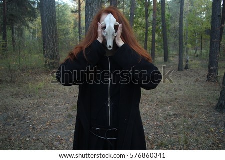 Young beautiful red-haired girl dressed like a witch in a black gown and dark clothes, with long hair, looks like a fox in the autumn forest