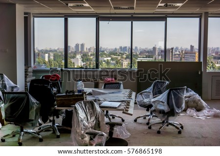 office preparing for moving. black office armchairs pack into clear package, meeting board are laying on the table, window without flowers and dirty floor as symbol of collecting things